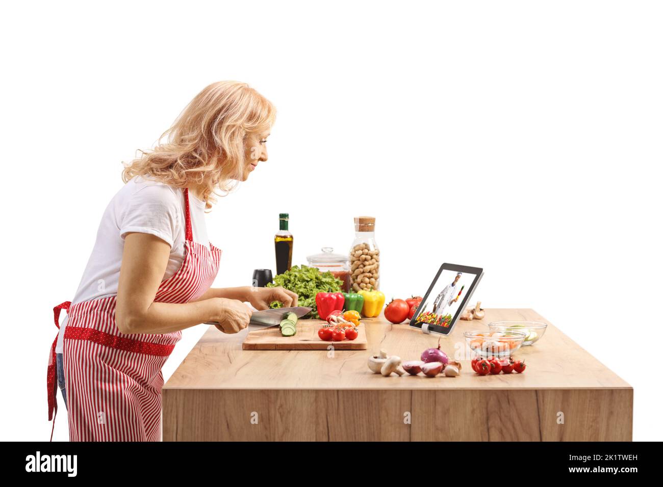 Side shot of a mature woman cooking and watching a video on a tablet isolated on white background Stock Photo
