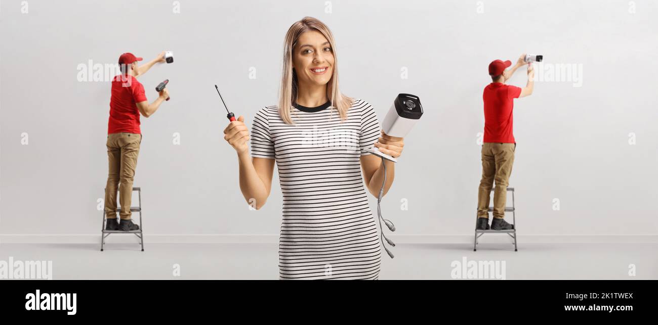 Workers installing cameras and a casual young woman holding cctv and drill Stock Photo