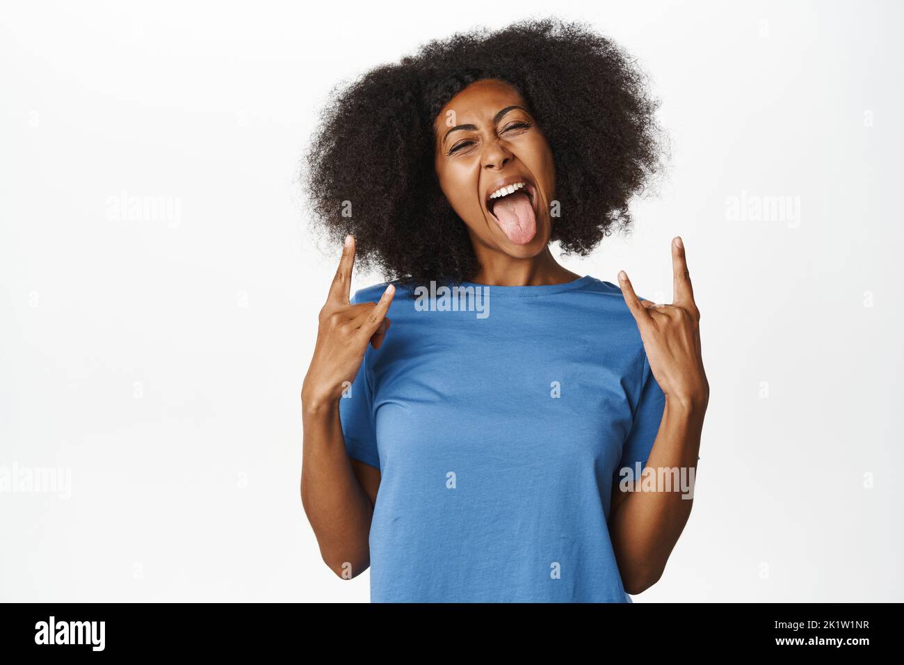 Enthusiastic Black female model, showing rock on, heavy metal party gesture, having fun, enjoying smth awesome, standing in blue t-shirt over white ba Stock Photo