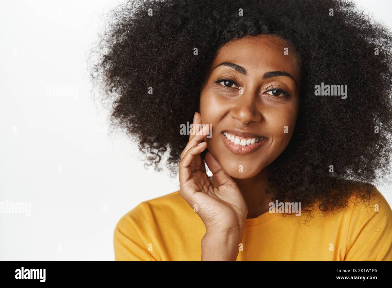 Close up portrait of beautiful, feminine african american woman smiling, touching face and looking happy. Concept of skin care, beauty and cosmetology Stock Photo