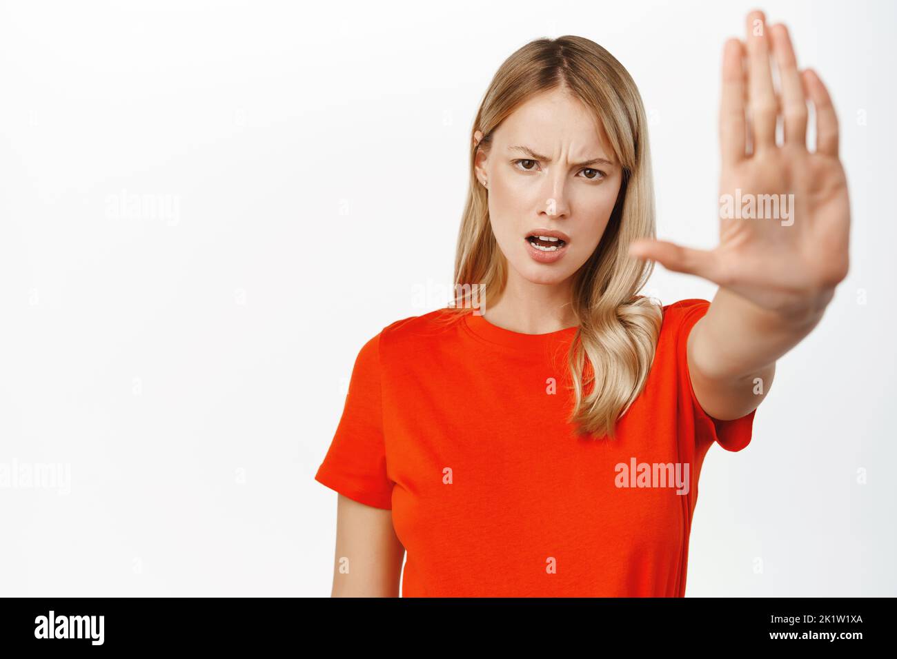 Portrait of serious young blond woman say stop, showing taboo, block refusal gesture, extending one arm forward, prohibit smth, forbid, standing over Stock Photo