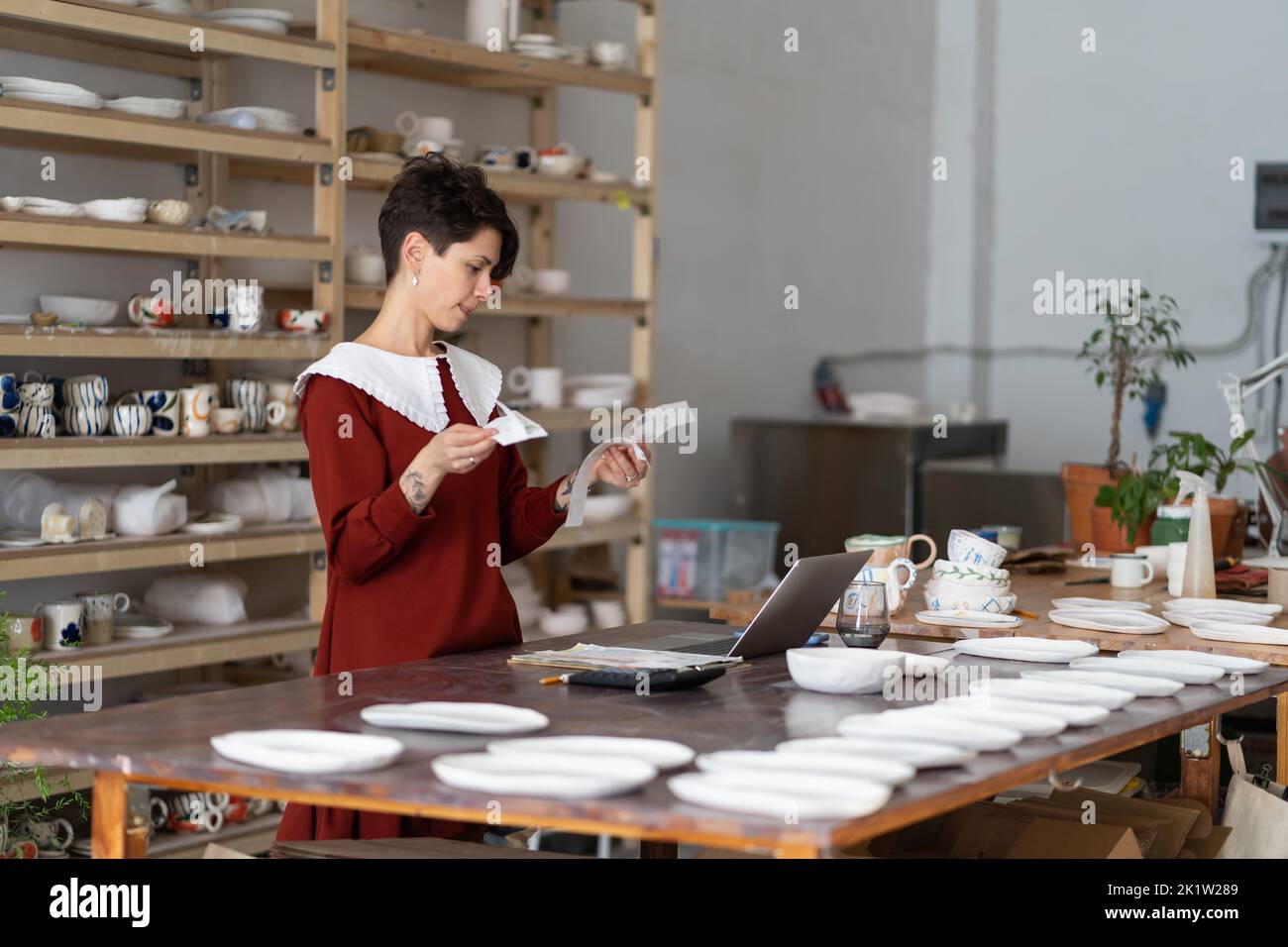 Female pottery studio owner looking at receipts calculating material costs to make ceramic product Stock Photo