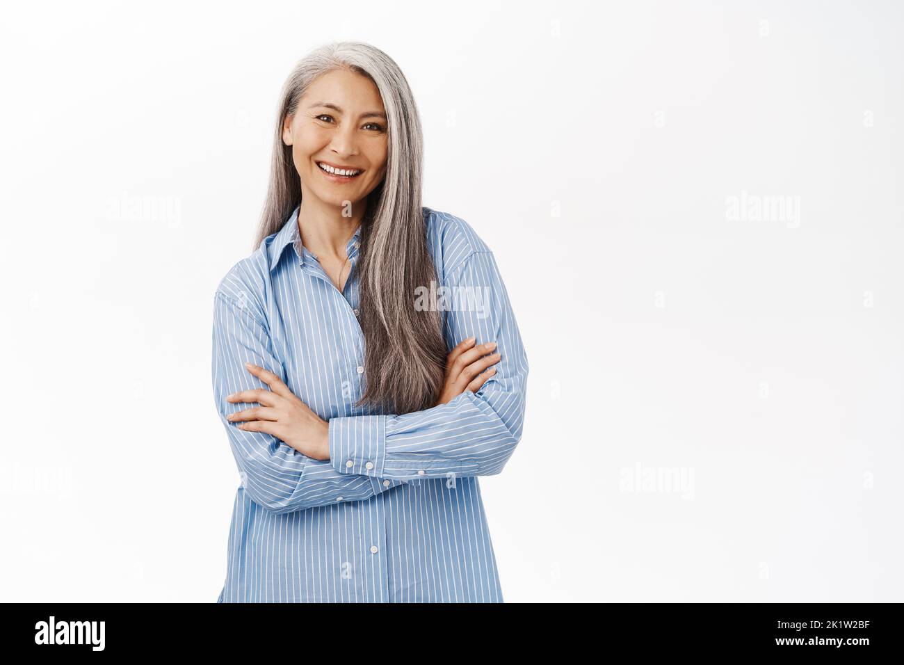 Smiling asian woman, senior lady looking with confidence, standing in power pose against white studio background. Stock Photo