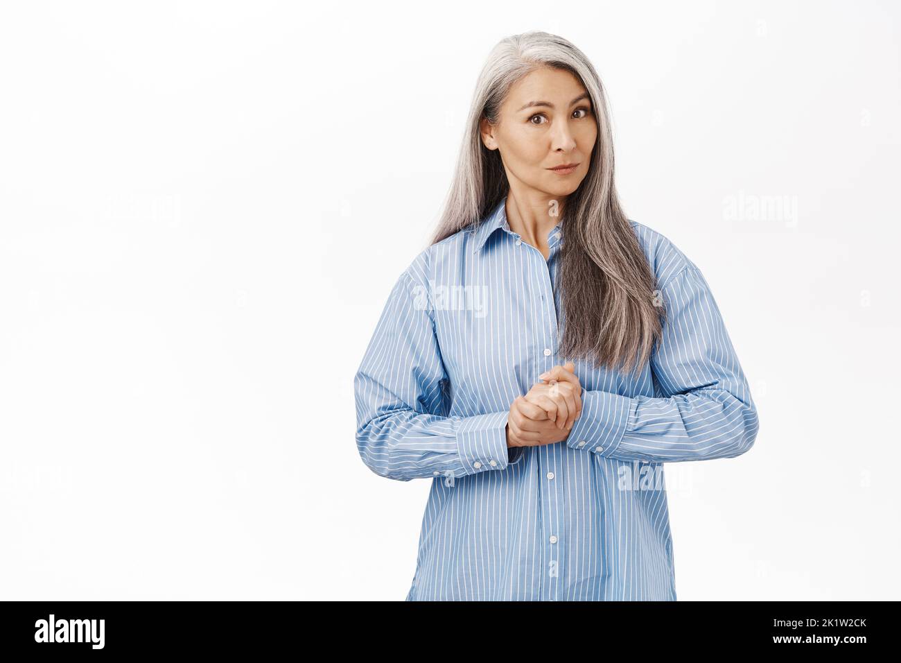Image of japanese senior woman, beautiful middle aged lady with grey hair, assisting, ready to help, consultating, standing over white background. Stock Photo