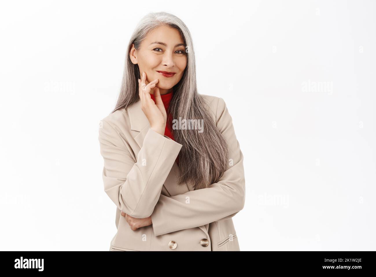 Portrait of beautiful asian female entrepreneur, businesswoman smiling, looking happy and confident, wearing stylish suit, standing over white backgro Stock Photo