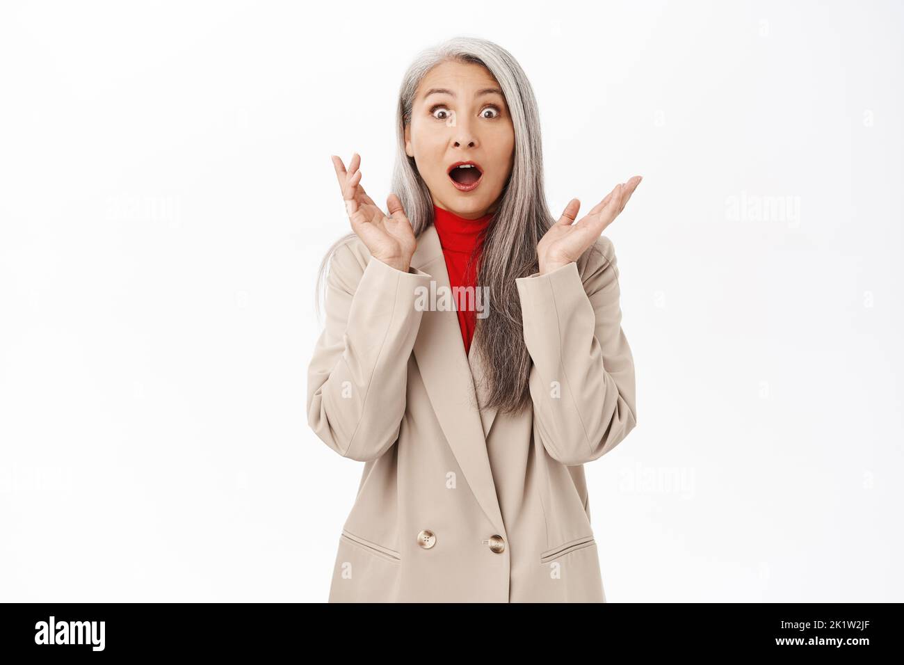Portrait of asian businesswoman, senior lady looking amazed, surprised wow face, standing over white background. Copy space Stock Photo