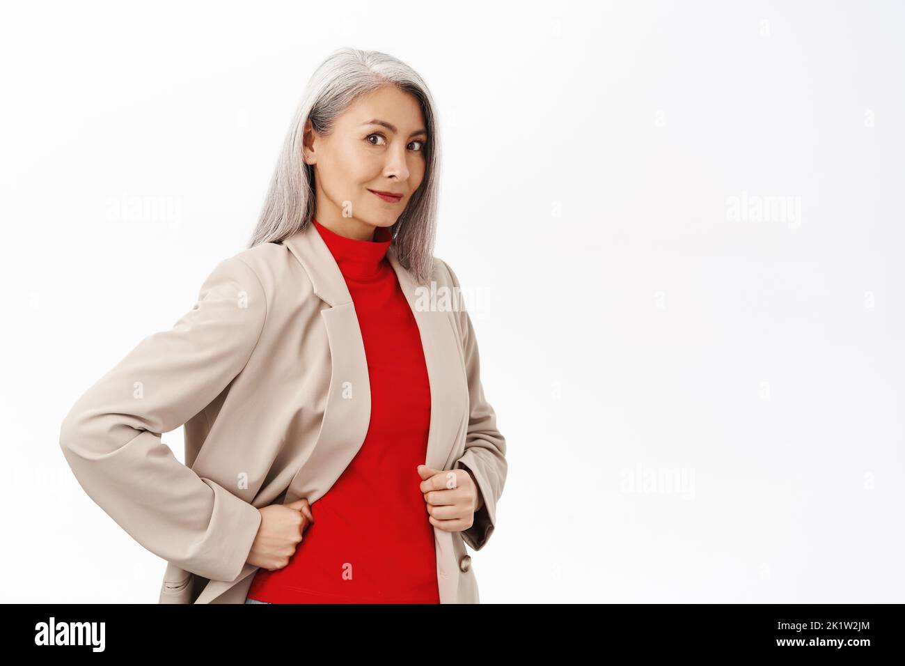Portrait of healthy and happy senior asian woman in stylish blazer, smiling and looking confident at camera, white smile, standing over white backgrou Stock Photo