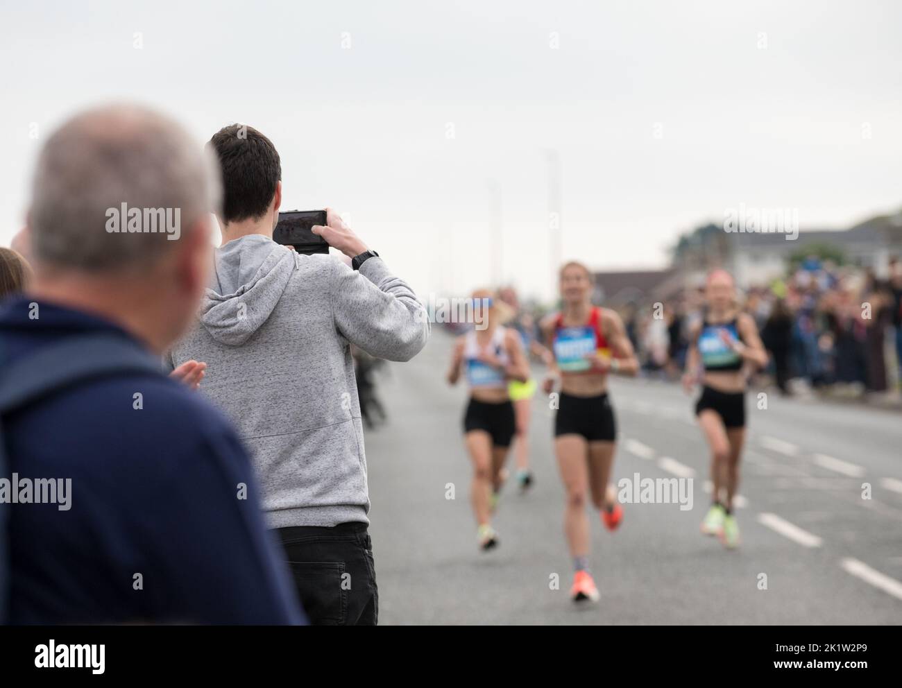 Male spectator taking a photograph of women competitors in the 2022 great North Run half marathon. Stock Photo