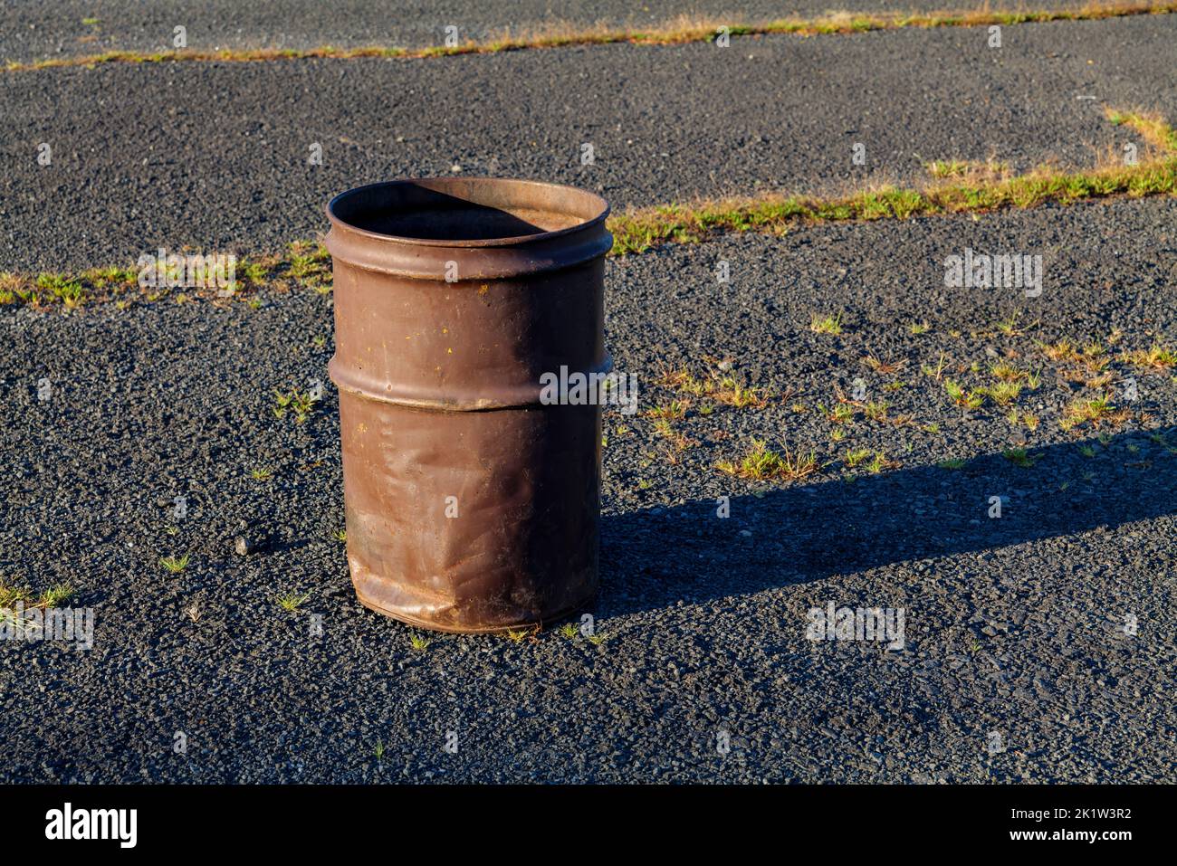 Garbage can in a metal barrel outside on asphalt at the parking lot