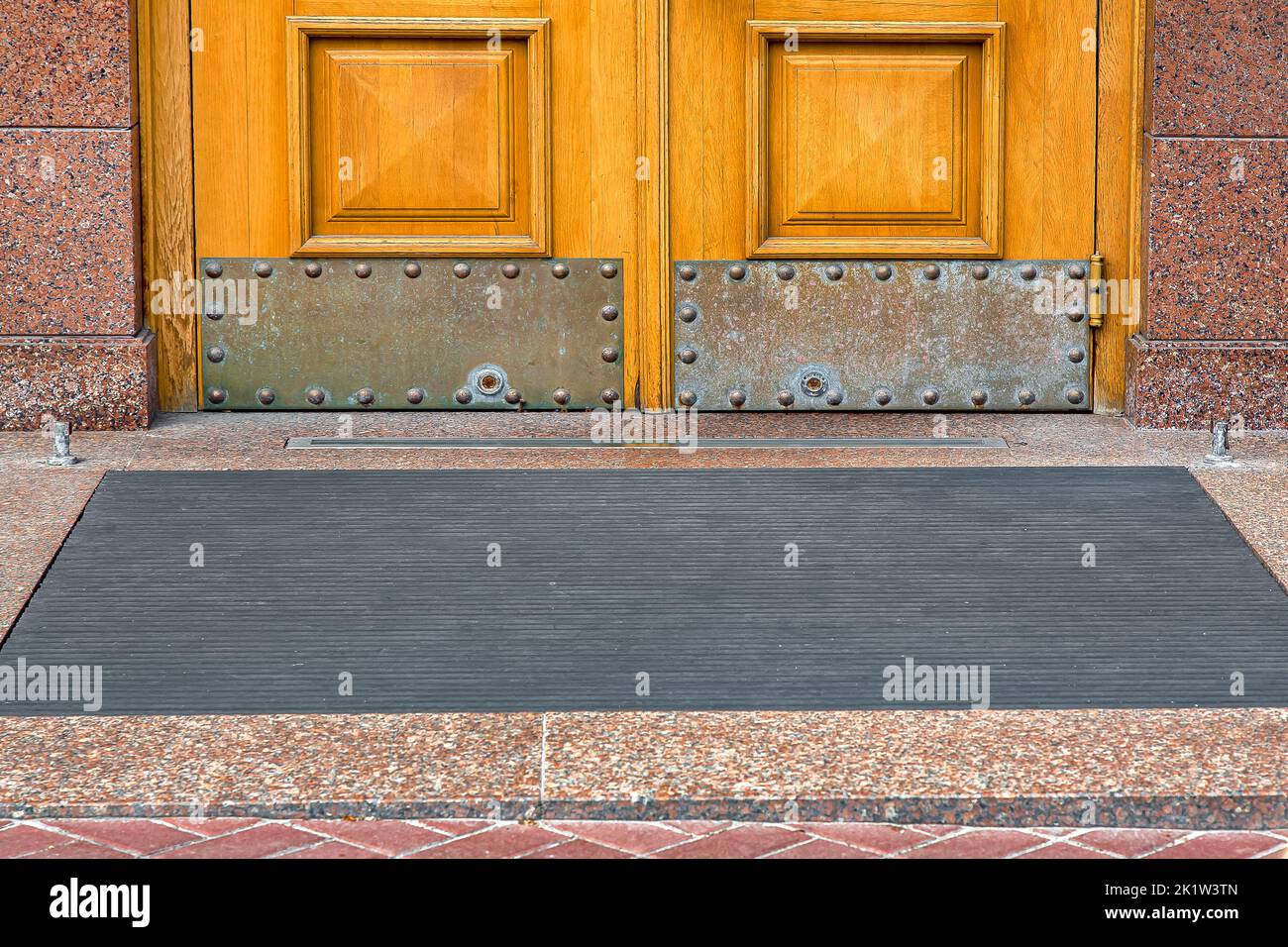 stone threshold with foot mat at the entrance door made of wood and granite stone facade cladding of old architecture building closeup front view on c Stock Photo