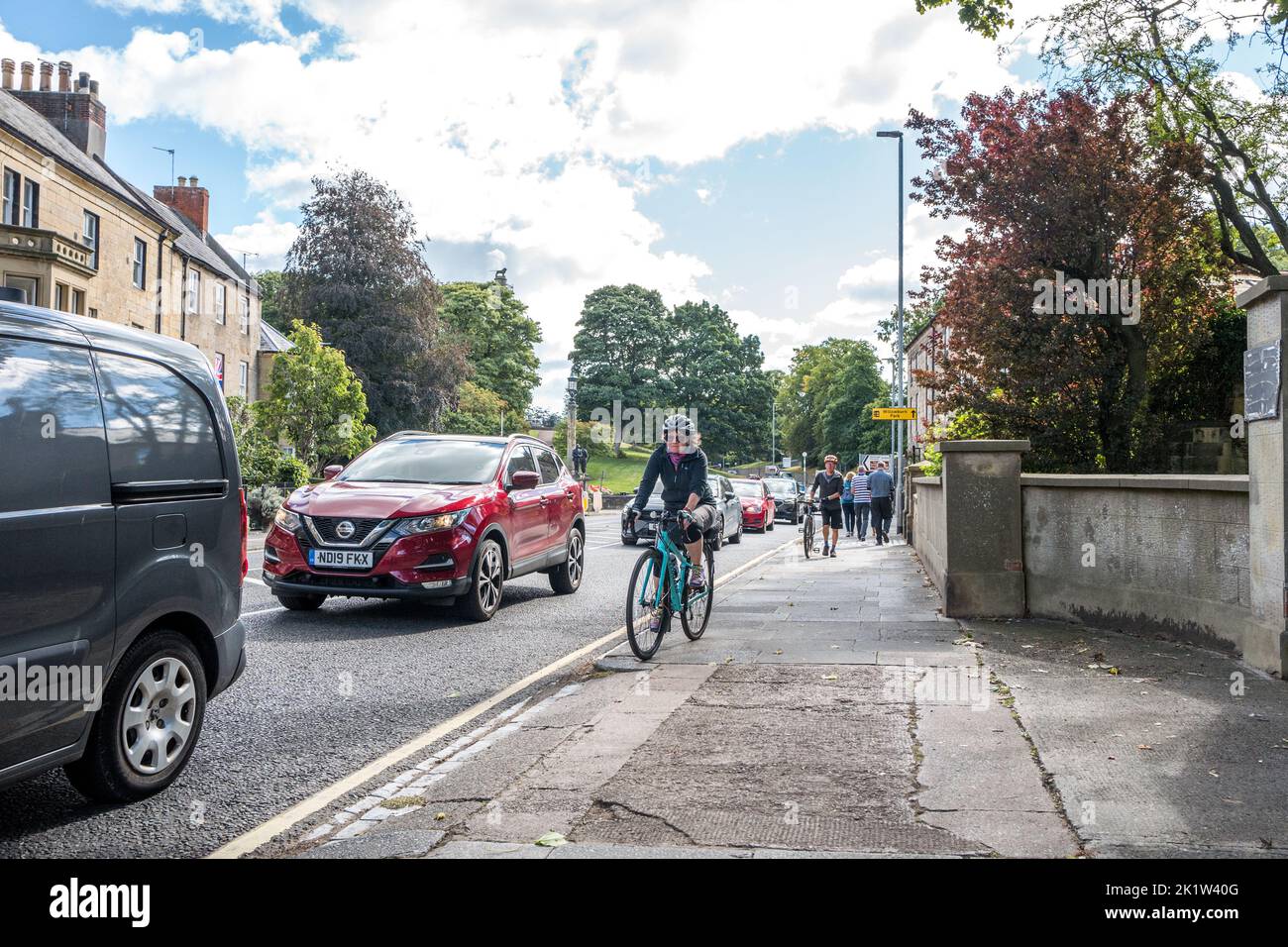 Female cyclist riding on the pavement at the side of a busy road in