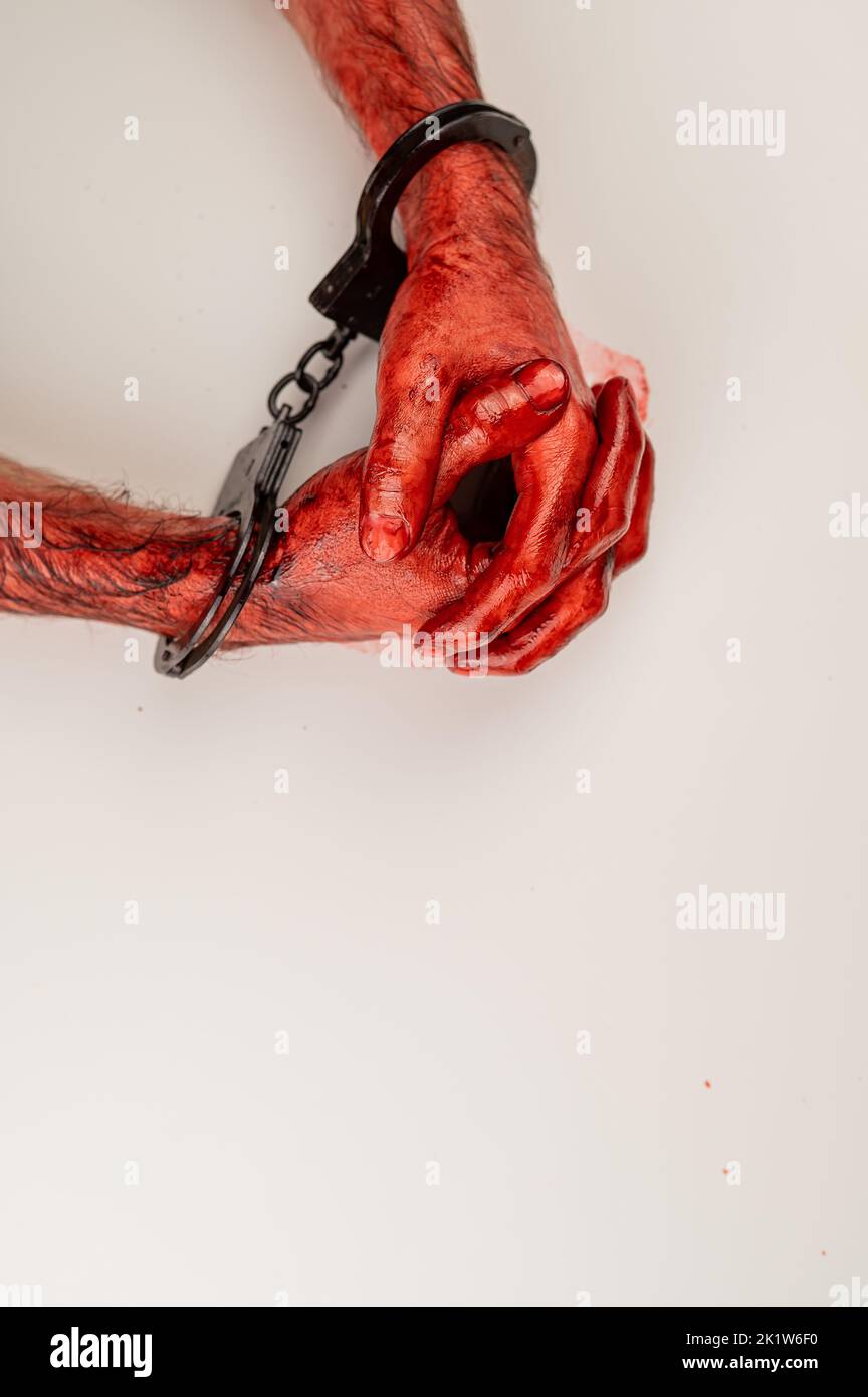 Bloodied male hands in handcuffs, folded on a white table. Stock Photo