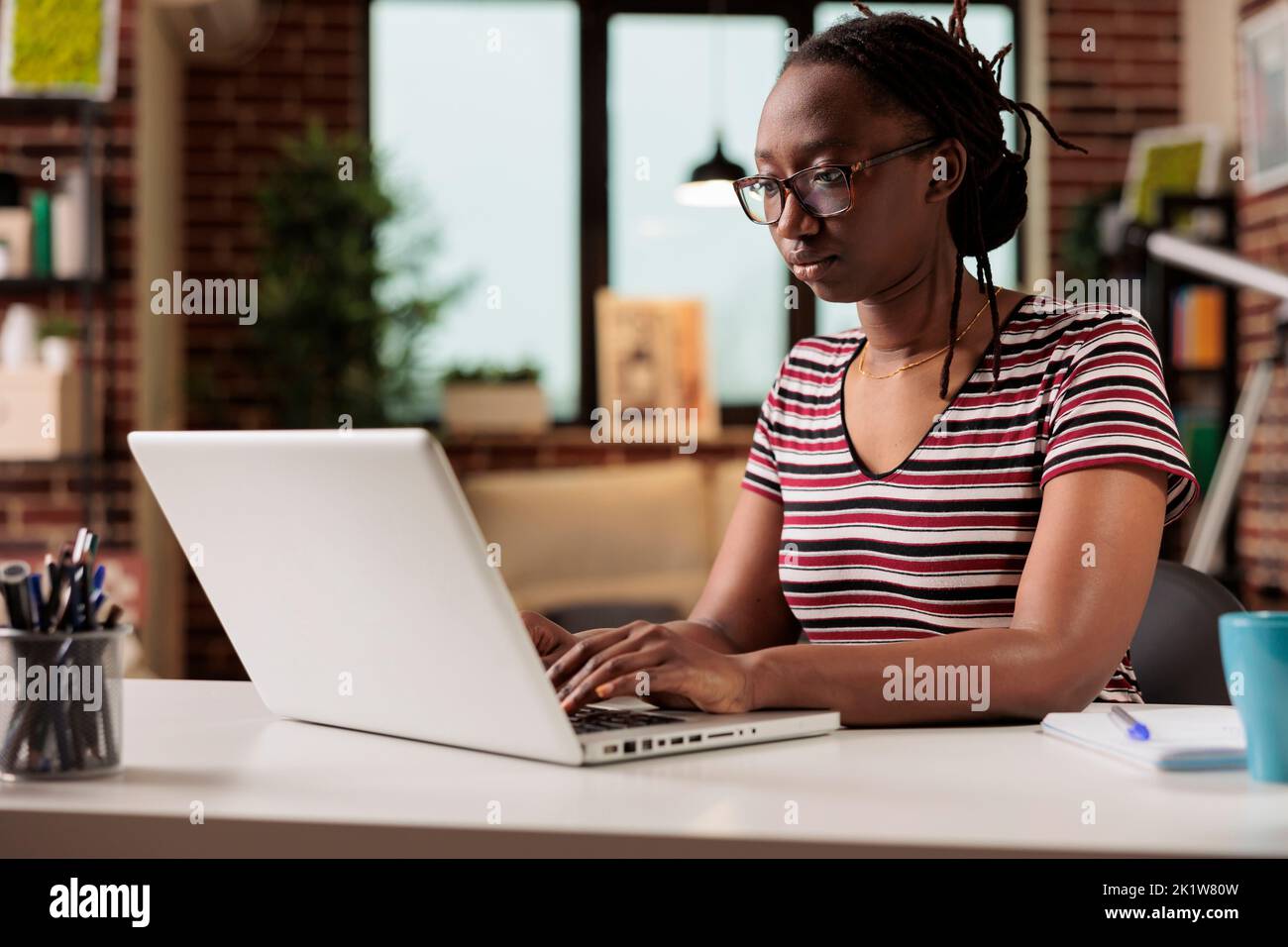 Freelancer working, typing on laptop keyboard, searching information on internet in home office. Employee writing message on computer, copywriting, sitting at workplace desk Stock Photo