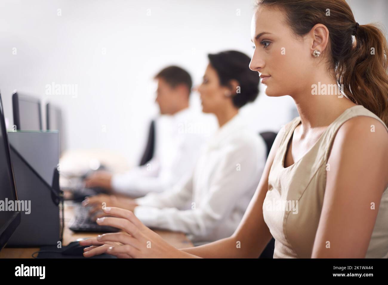 Fully focussed on her work. an attractive young office worker at her computer with her colleagues in the background. Stock Photo