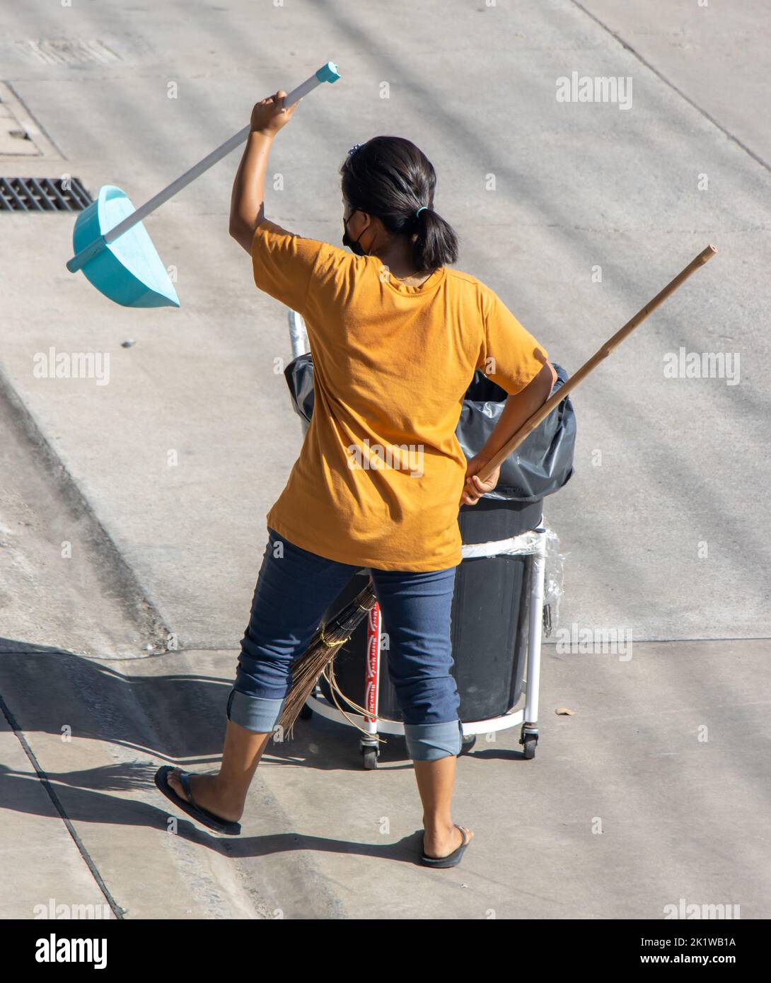 SAMUT PRAKAN, THAILAND, MAY 26 2022, A young woman with a broom and a shovel cleans the street Stock Photo
