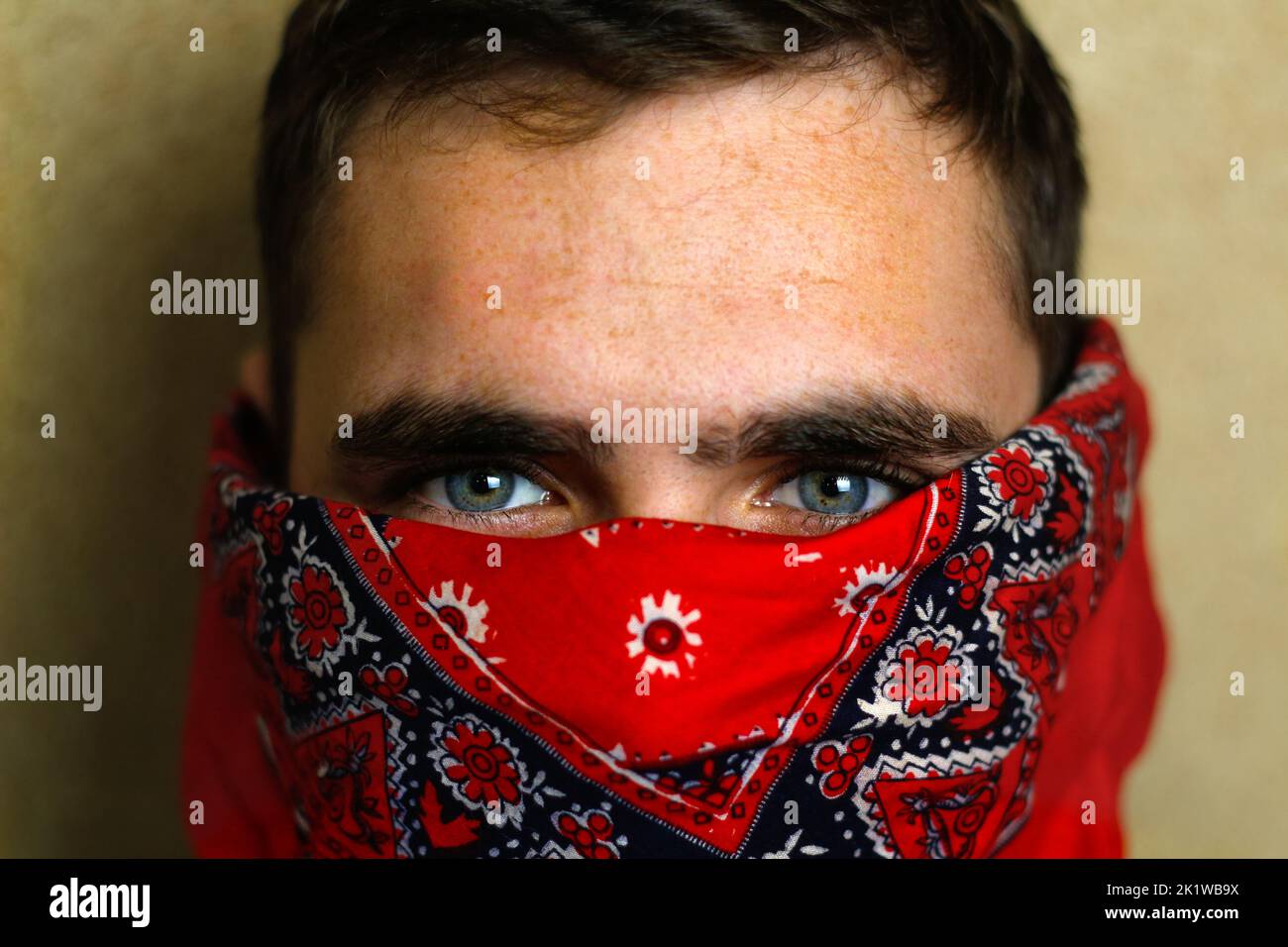 Defocus young man in red bandana. Closeup blue dark eyes. Man with his face hidden behind a bandanna stares balefully at the camera. Out of focus. Stock Photo