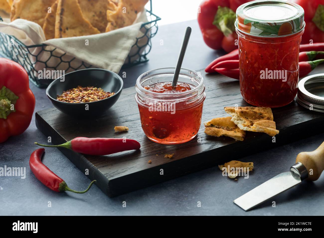 Red hot pepper jelly in a small jar surrounded by ingredients used to make it. Stock Photo