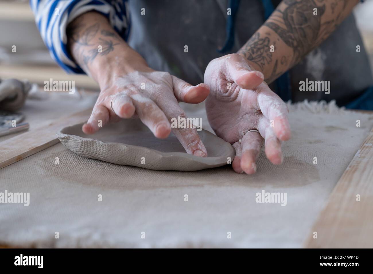 Closeup of working table in ceramics studio with female master shaping wet clay plate. Hobby concept Stock Photo