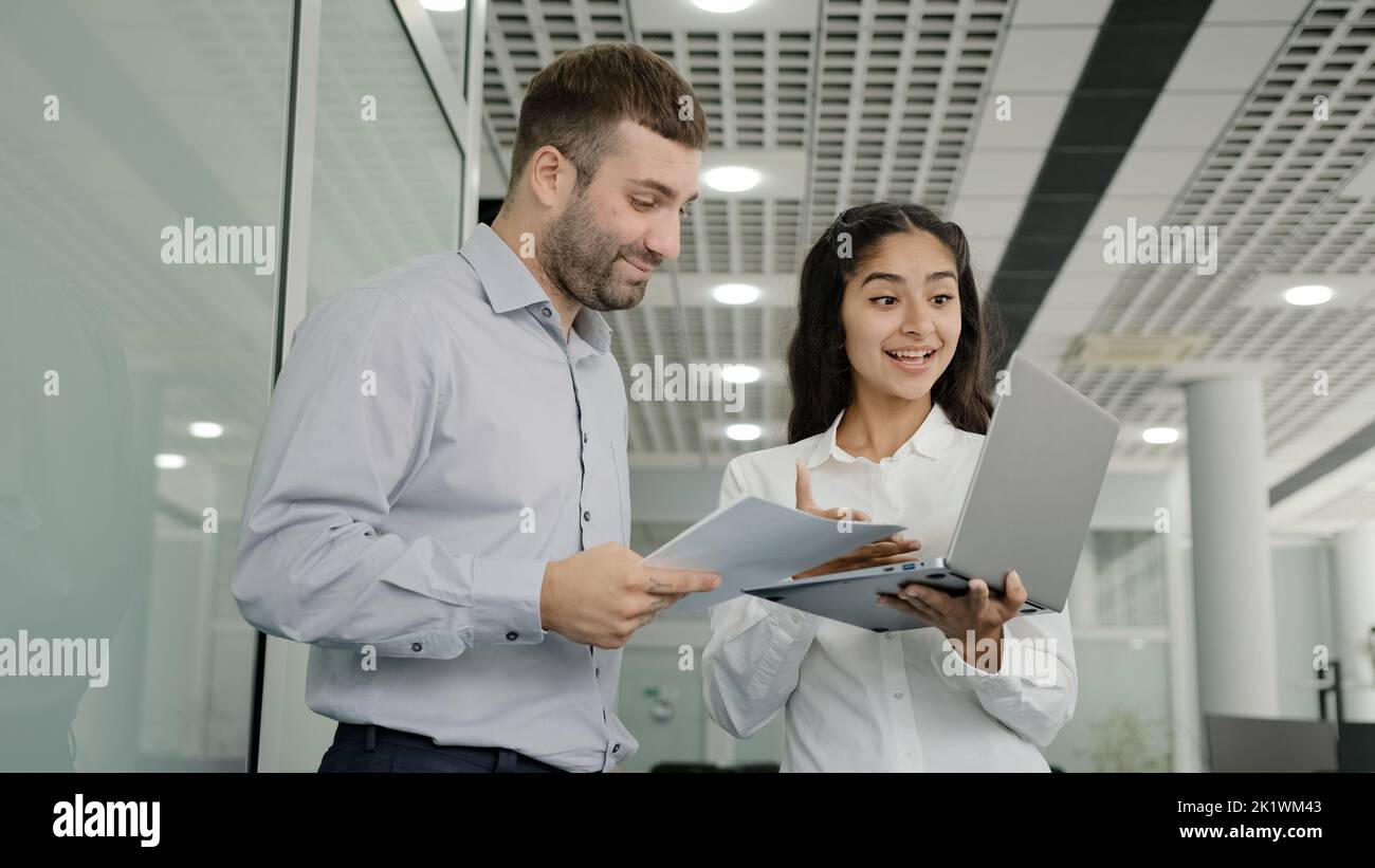 Young female trainee showing presentation on laptop to male tutor diverse colleagues communicate in office discussing project strategy girl consultant Stock Photo