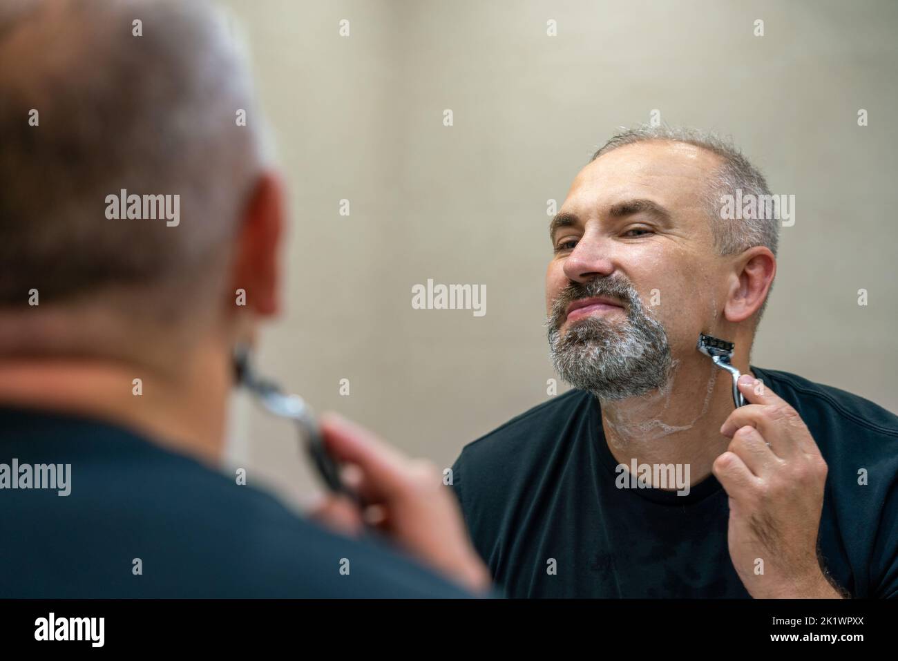 Middle-aged handsome man using razor in bathroom Stock Photo