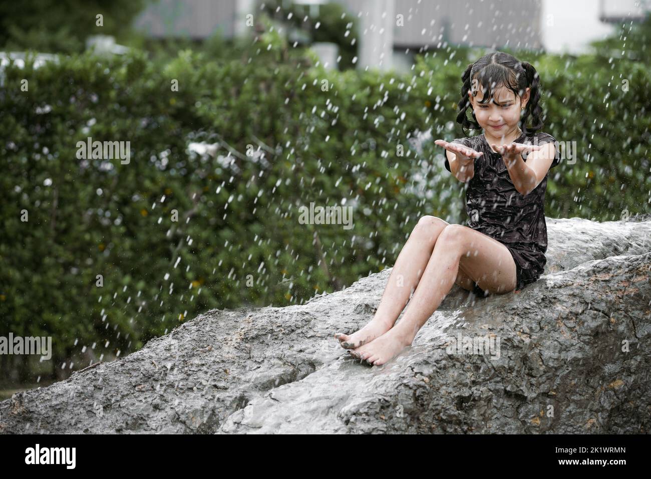 Cheerful child girl playing on heap of wet soil during raining in rainy season. Stock Photo