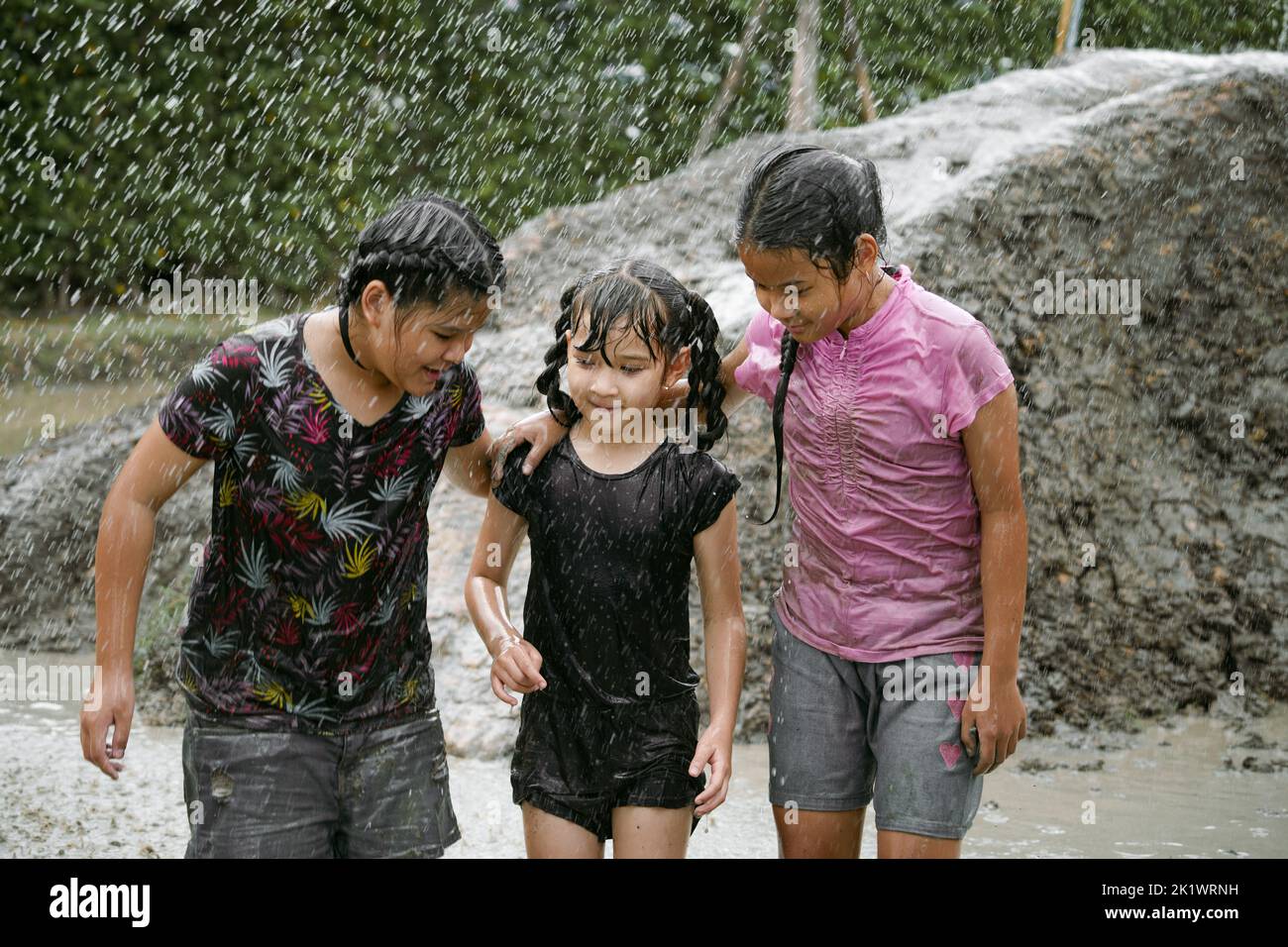 Group of happy children girl playing in wet mud puddle during raining in rainy season Stock Photo
