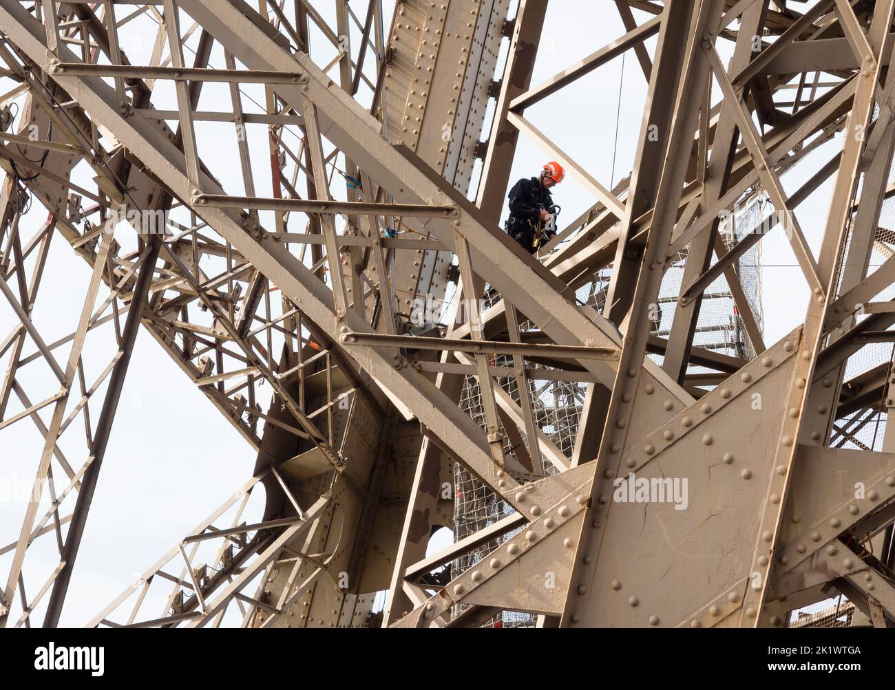 A painter on a rope is climbing the steel framework of Paris Eiffel tower. Stock Photo