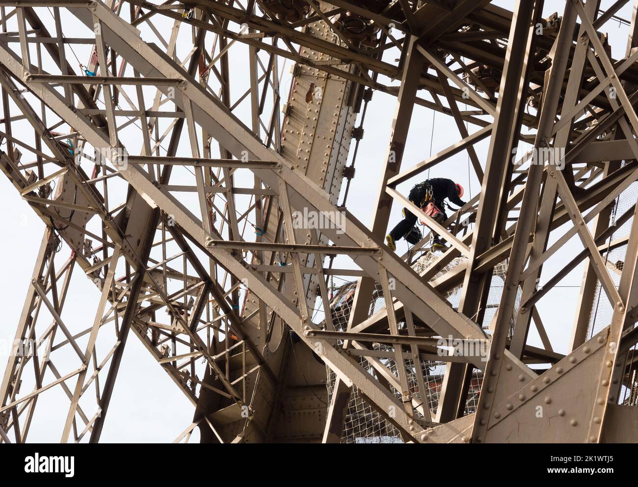 A painter on a rope is climbing the steel framework of Paris Eiffel tower. Stock Photo