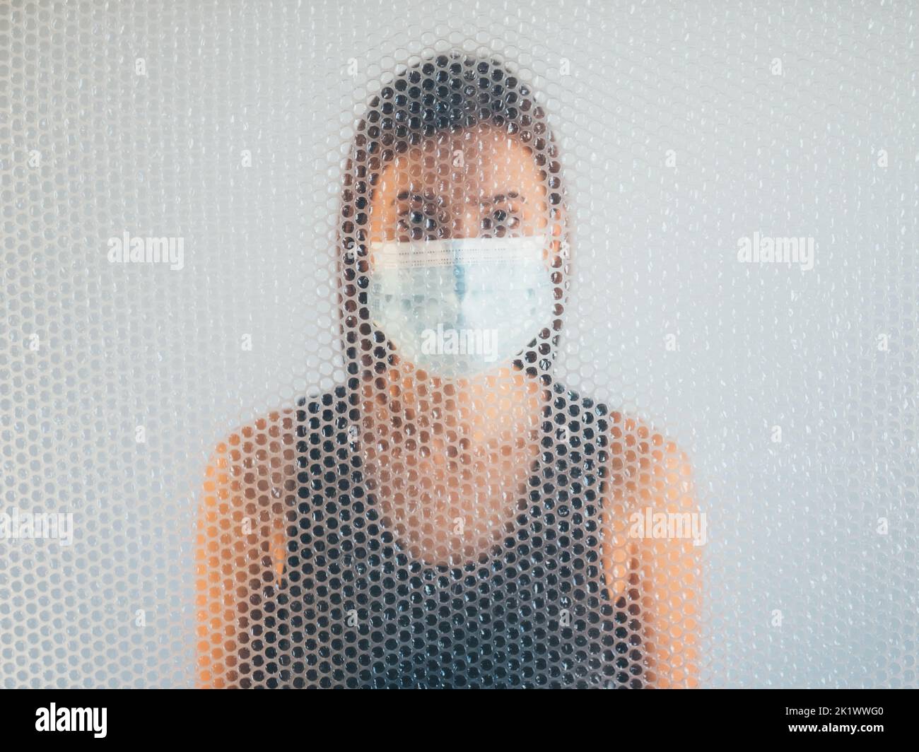 Air pollution. Defocused portrait. Respiratory disorder. Concerned woman in protective face mask behind transparent polyethylene bubble wrap texture d Stock Photo