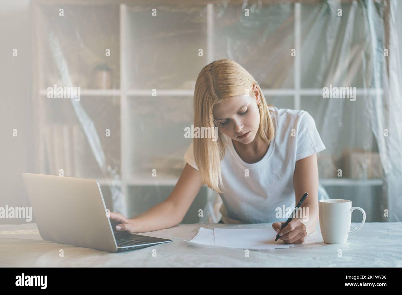 Remote job. Distance work. Pandemic furlough. Tired freelancer keyworker woman busy with project alone with laptop at light virtual office covered wit Stock Photo