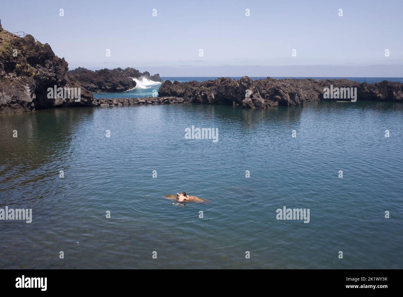 Natural pool at Seixal on the North coast of Madeira with boy holding on to wooden log Stock Photo