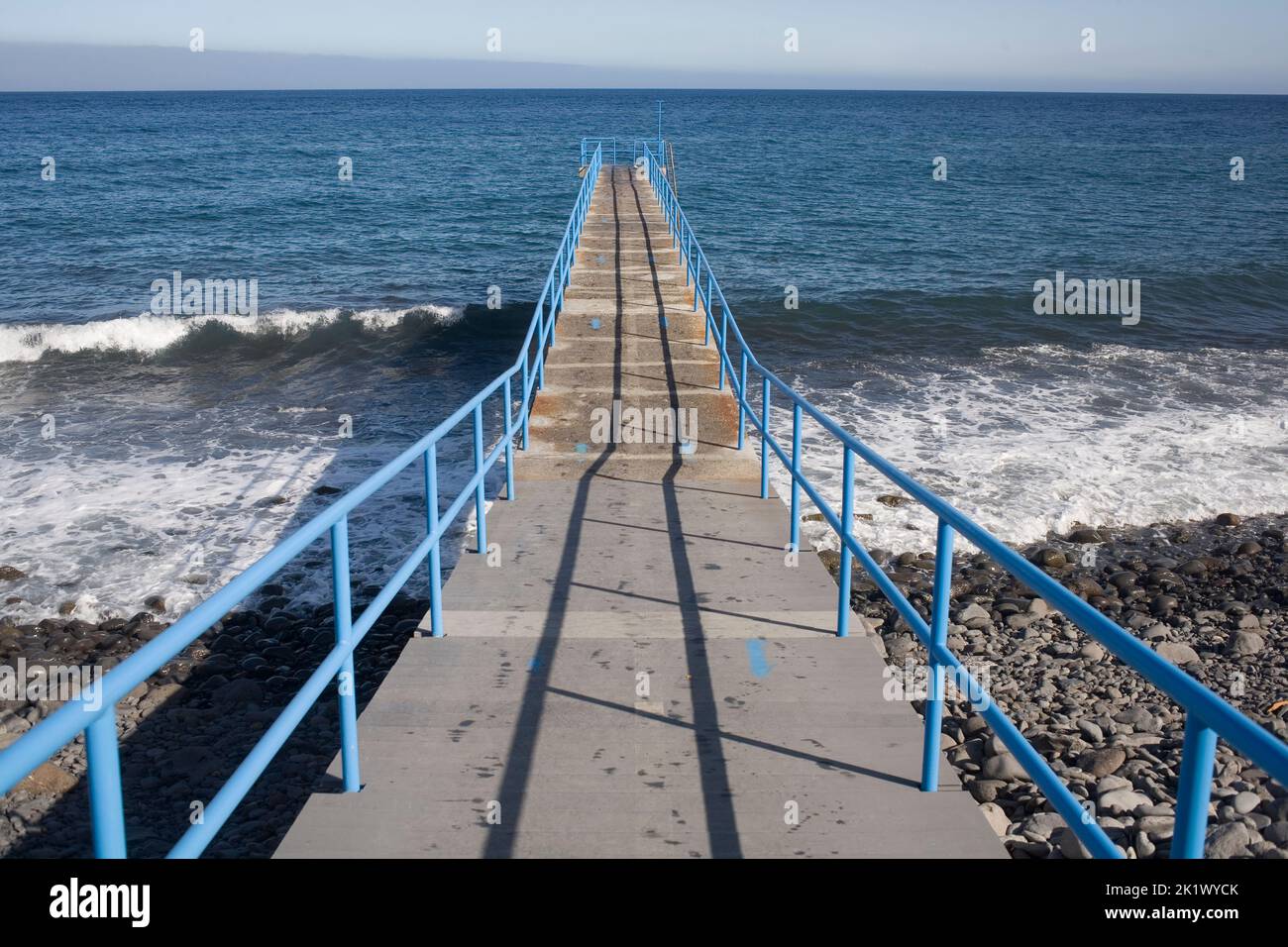 Concrete walkway with blue metal railing providing swimming access at Santa Cruz's Palmeiras beach Stock Photo