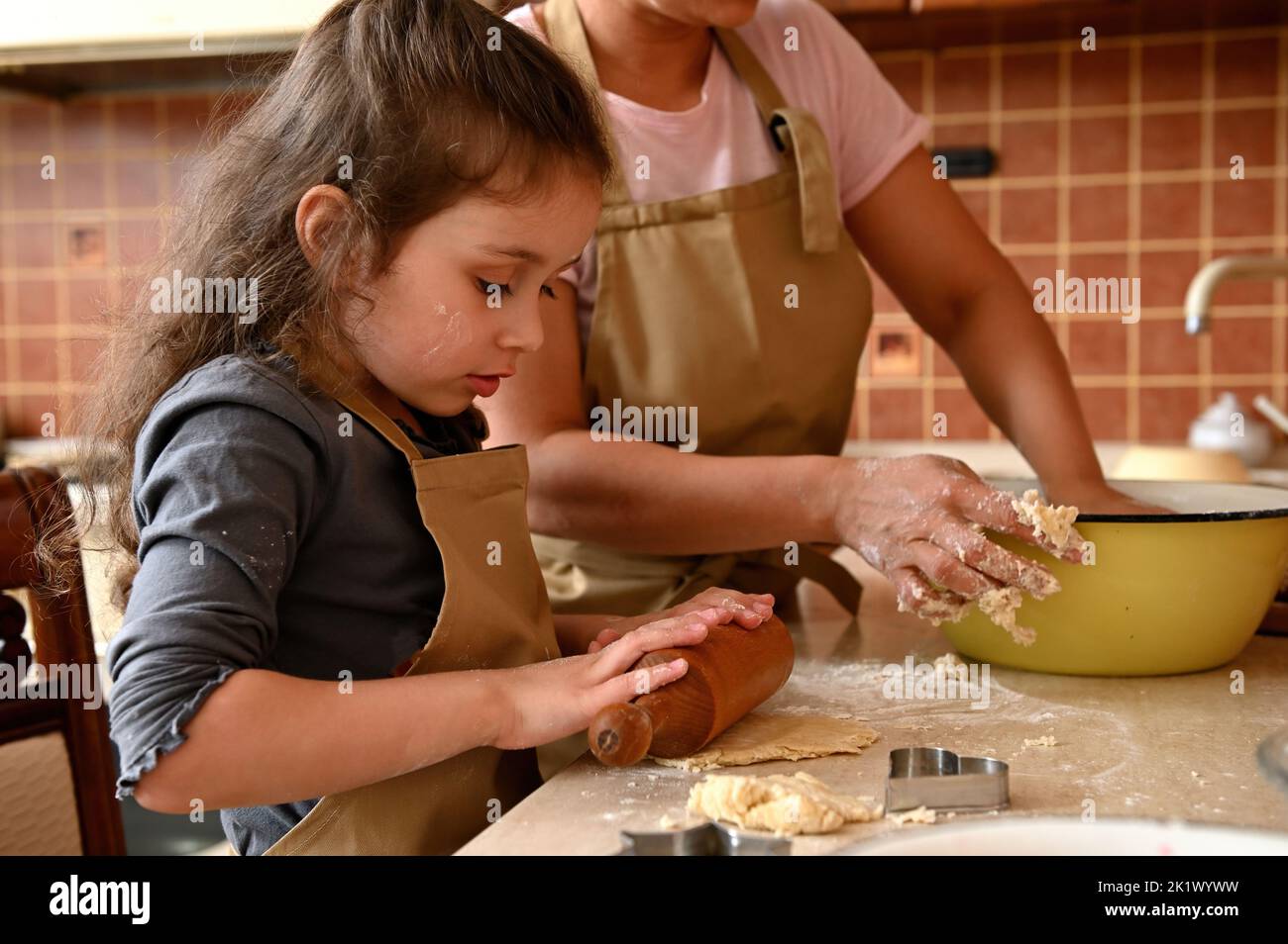 Close-up. Beautiful little girl kneads and rolls out dough with a ...