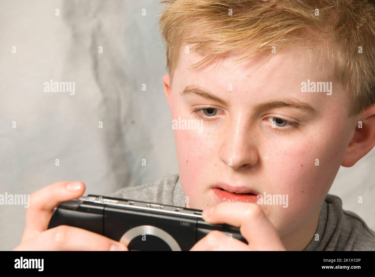 A teenage boy is engrossed while playing a Sony PSP handheld gaming console Stock Photo