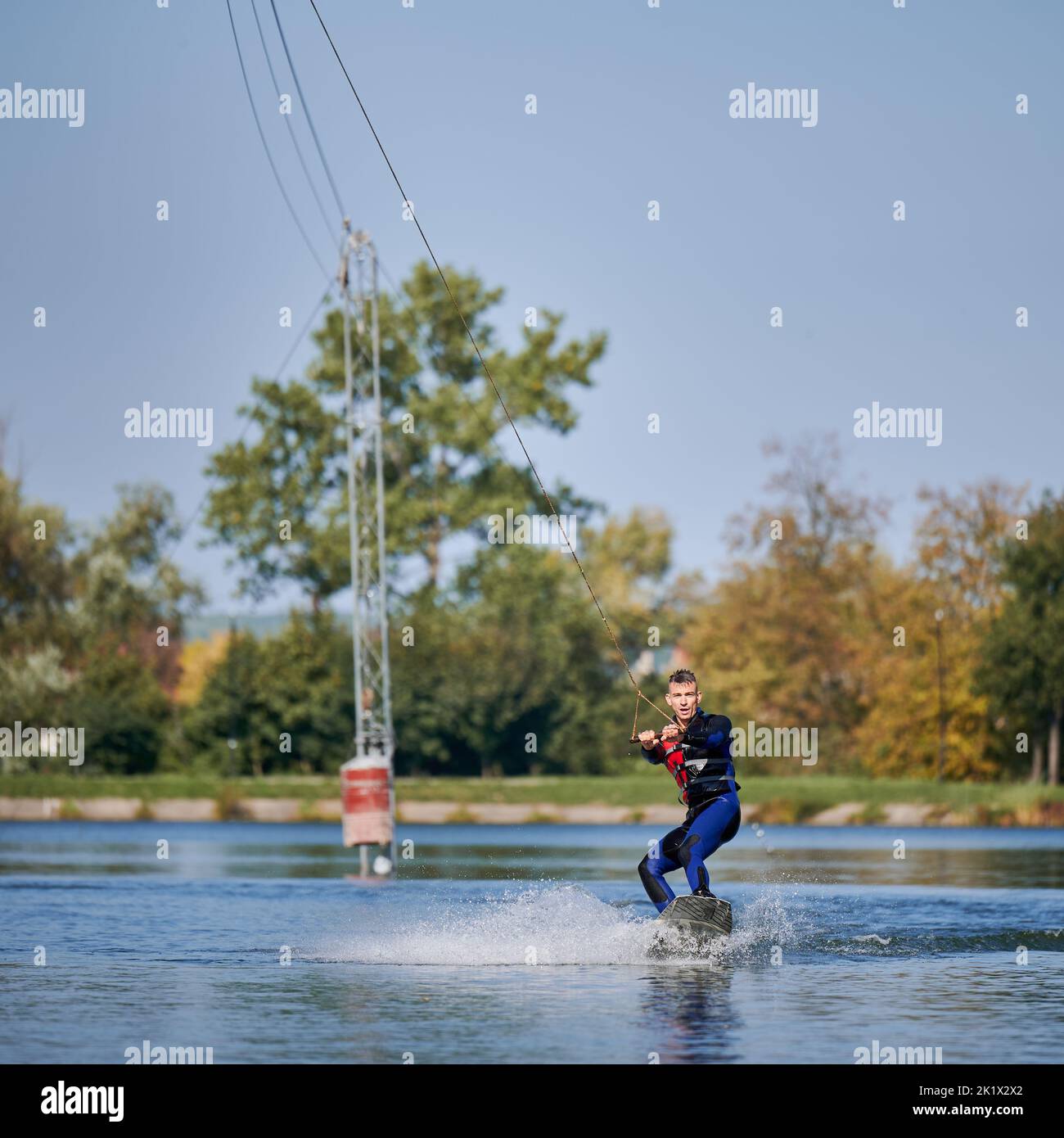Wakeboarder surfing on lake. Young man surfer having fun wakeboarding in the cable park. Water sport, outdoor activity concept. Stock Photo
