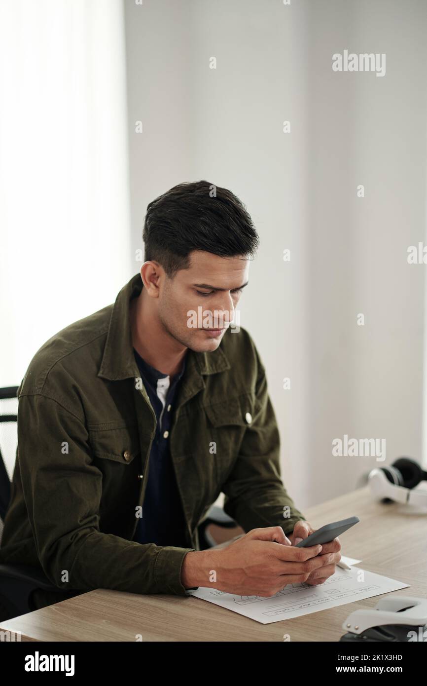 Serious software developer checking text messages on smartphone instead of working on project Stock Photo