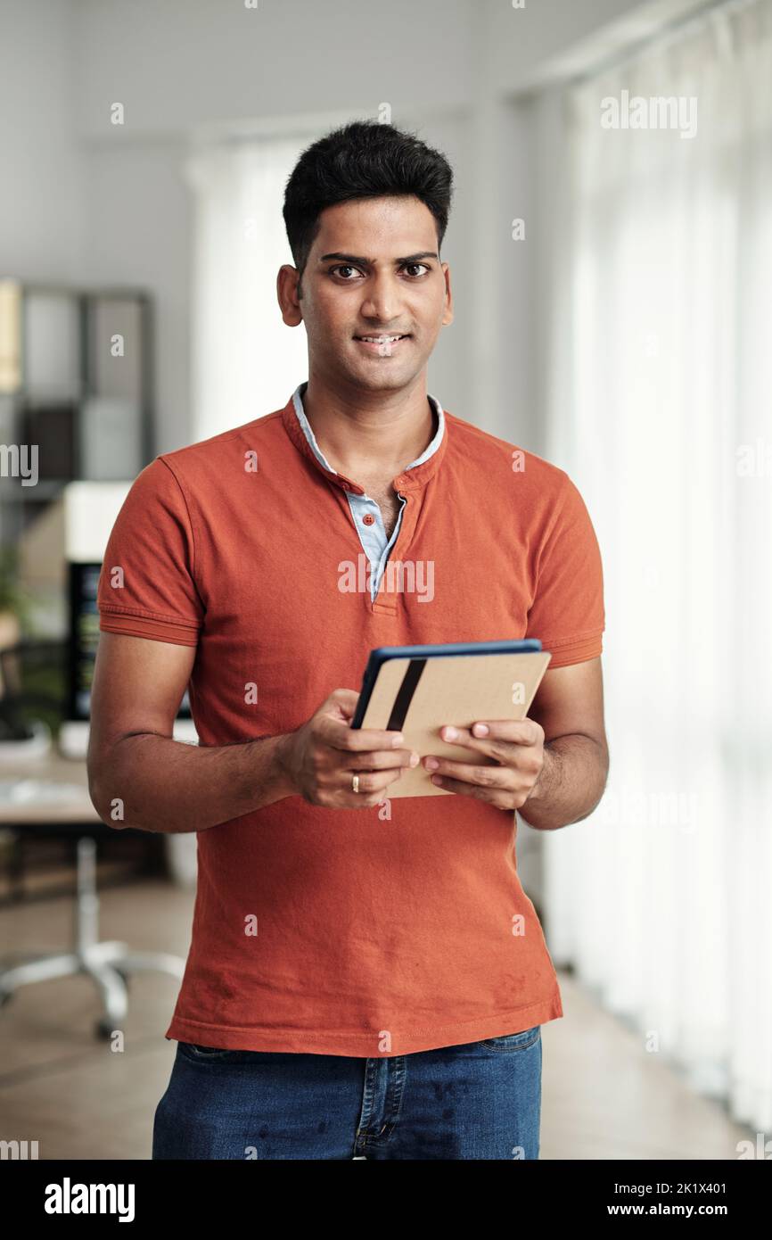 Positive software engineer holding tablet computer and smiling at camera Stock Photo