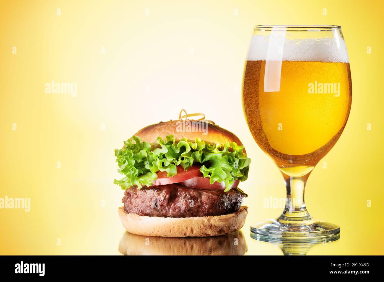 Beer glass and hamburger over color background Stock Photo