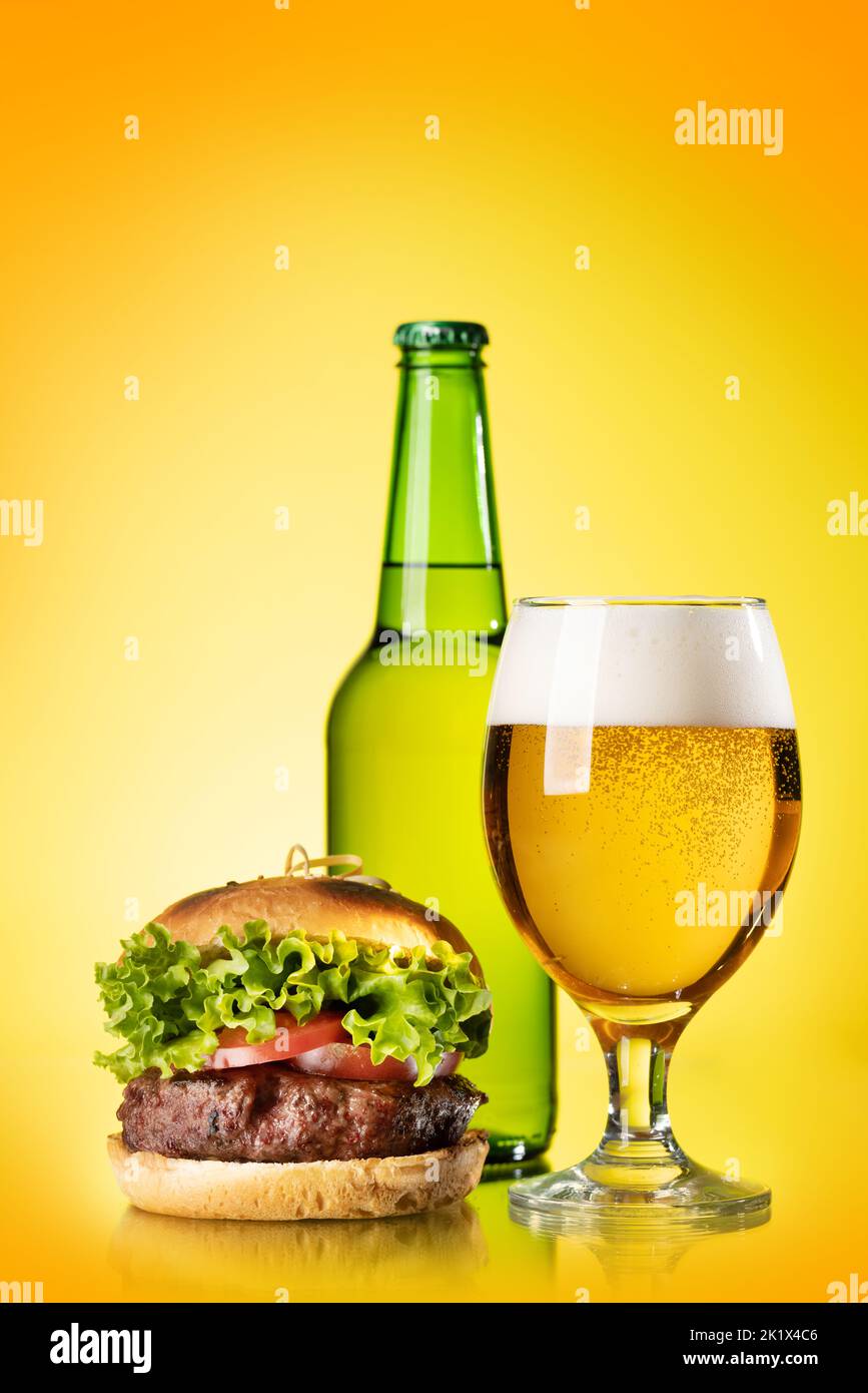 Beer glass, bottle and hamburger over color background Stock Photo