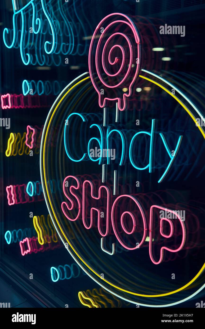 A closeup shot of a neon sign with &ldquo;Candy SHOP&rdquo; text and a lollipop on