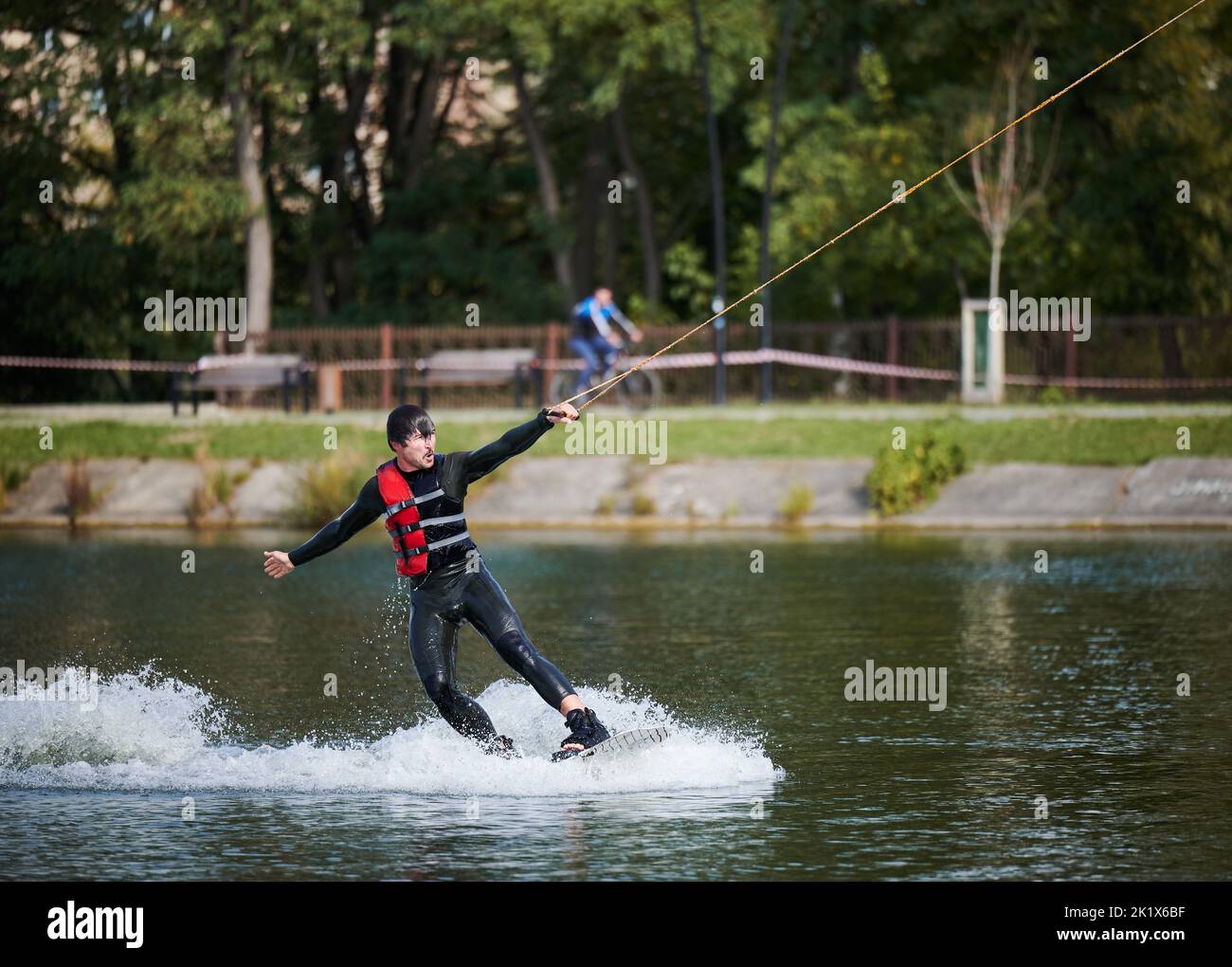 Wakeboarder surfing on lake. Young man surfer having fun wakeboarding in the cable park. Water sport, outdoor activity concept. Stock Photo