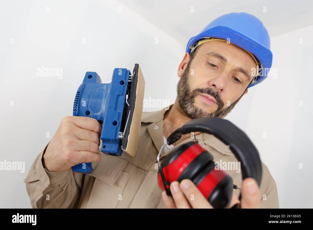 builder considering wearing earmuffs while using sander Stock Photo