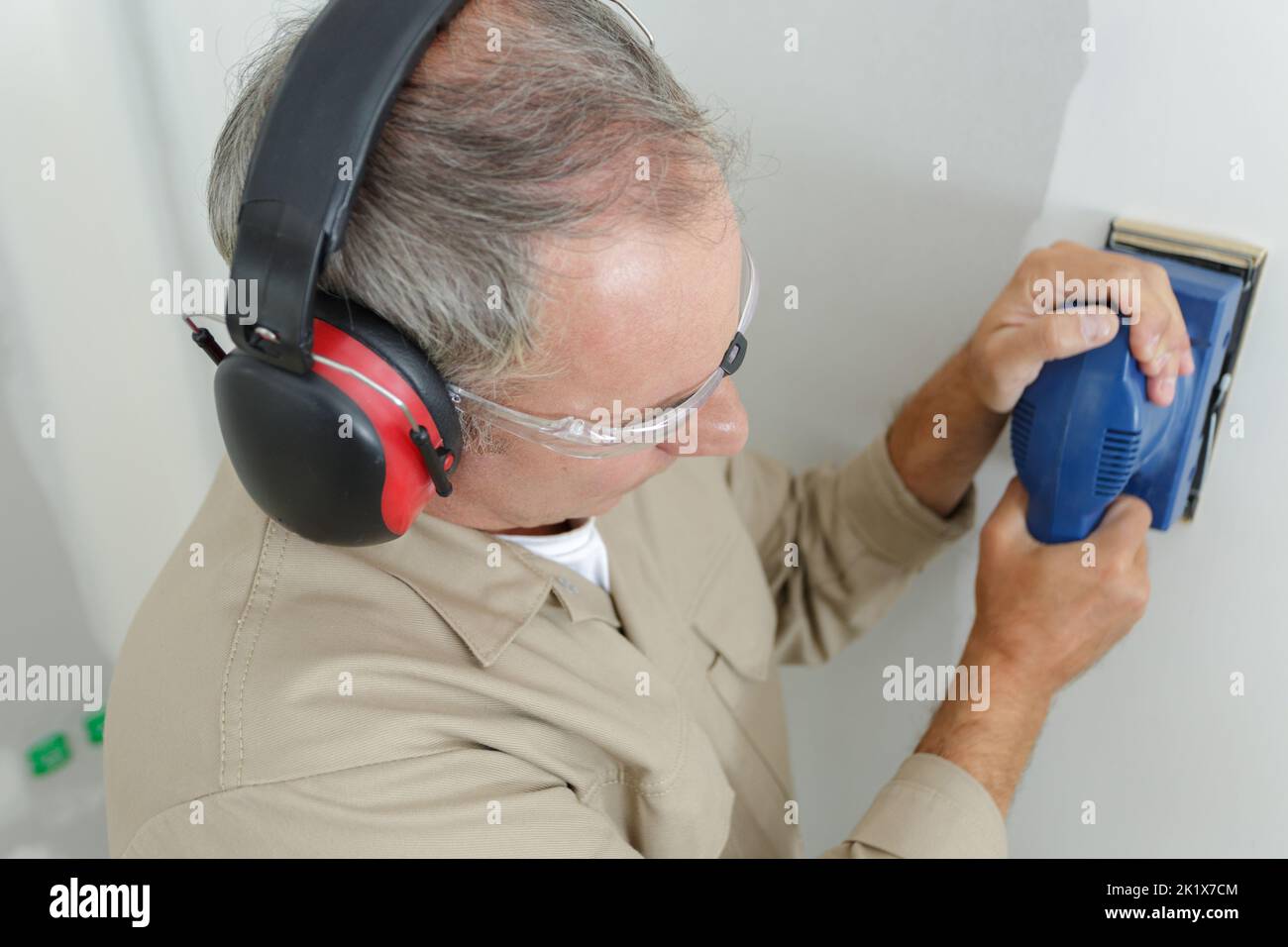 builder in hardhat sanding wall indoors Stock Photo
