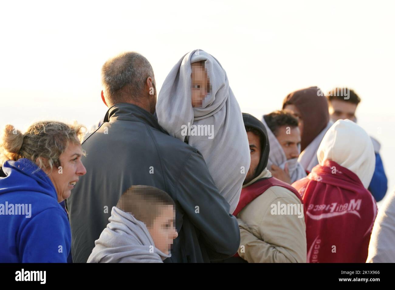 EDITORS NOTE Children's faces have been pixelated as the PA Picture Desk has been unable to gain the necessary permission to photograph a child under 16 on issues involving their welfare. A man carries a young child as a group of people thought to be migrants walk up the beach in Dungeness, Kent, after being rescued in the Channel by the RNLI following following a small boat incident. Picture date: Wednesday September 21, 2022. Stock Photo