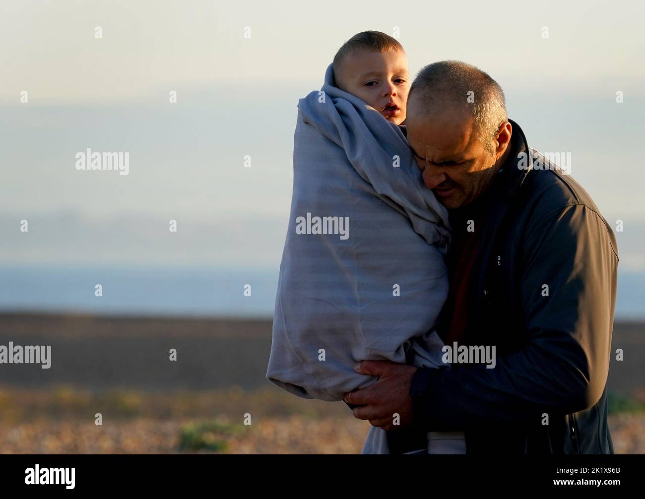 EDITORS NOTE: The PA Picture Desk has been unable to gain the necessary permission to photograph children under 16 on issues involving their welfare. This image has been provided unpixelated for customers to pixelate in their own style. A man carries a young child as a group of people thought to be migrants walk up the beach in Dungeness, Kent, after being rescued in the Channel by the RNLI following following a small boat incident. Picture date: Wednesday September 21, 2022. Stock Photo