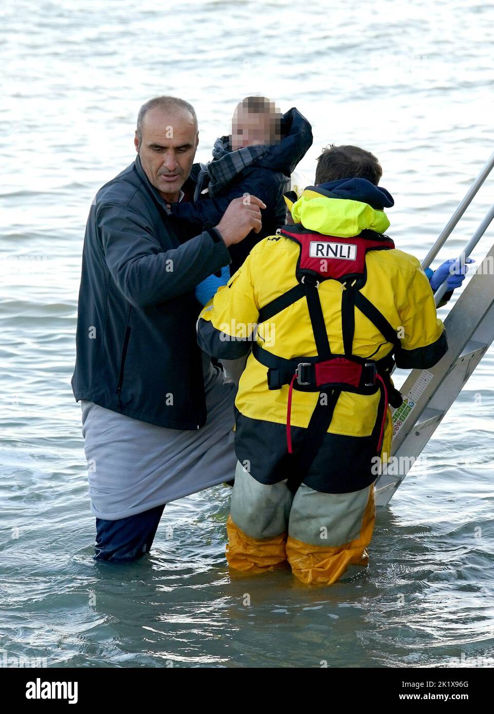 EDITORS NOTE Children's faces have been pixelated as the PA Picture Desk has been unable to gain the necessary permission to photograph a child under 16 on issues involving their welfare. A man carries a young child as a group of people thought to be migrants are helped to shore in Dungeness, Kent, after being rescued in the Channel by the RNLI following following a small boat incident. Picture date: Wednesday September 21, 2022. Stock Photo