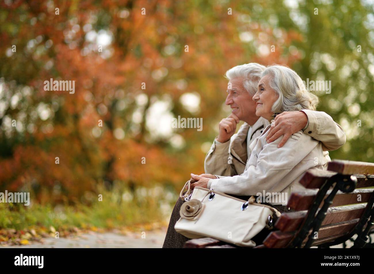 Beautiful elderly couple sitting together on a bench in autumn Stock Photo