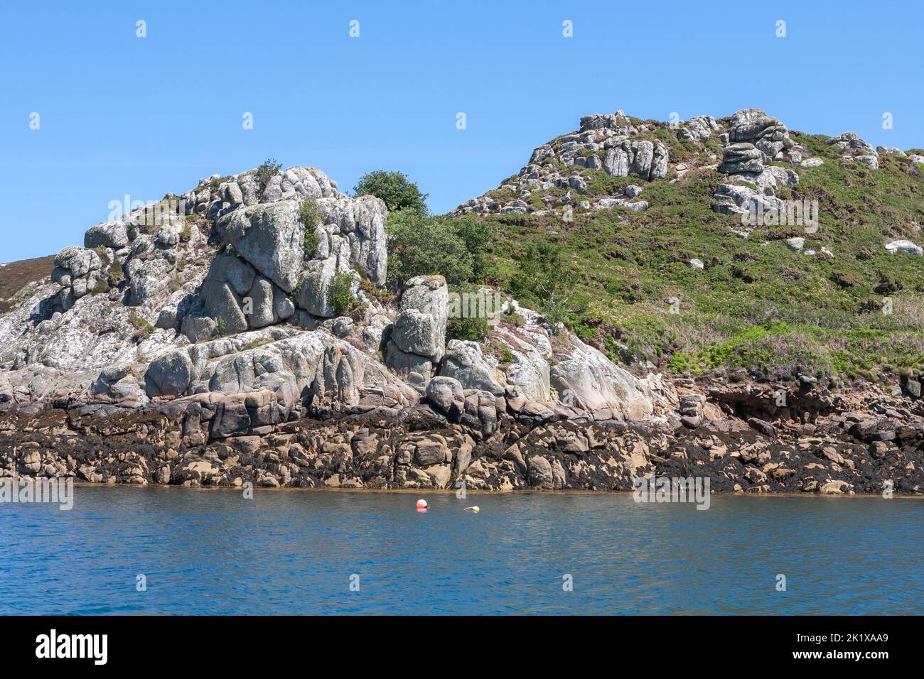 The coast of the island of Tresco from a yacht in New Grimsby Sound between Tresco and Bryher, Isles of Scilly, UK on a calm Summer's day. Stock Photo