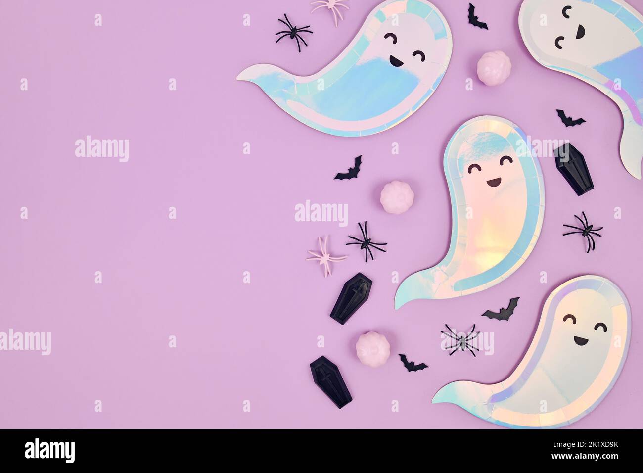 Cute pastel colored Halloween party flat lay with ghost shaped plates, spiders, pumpkins and coffins on violet background Stock Photo