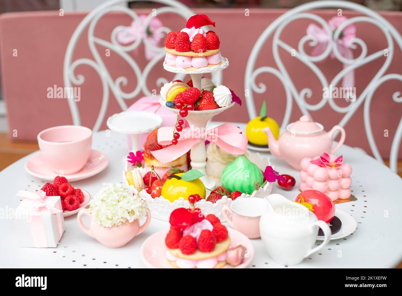 Abundant assortment of sugar dessert treats with present box and teapot on white table with chairs in cafe or restaurant Stock Photo
